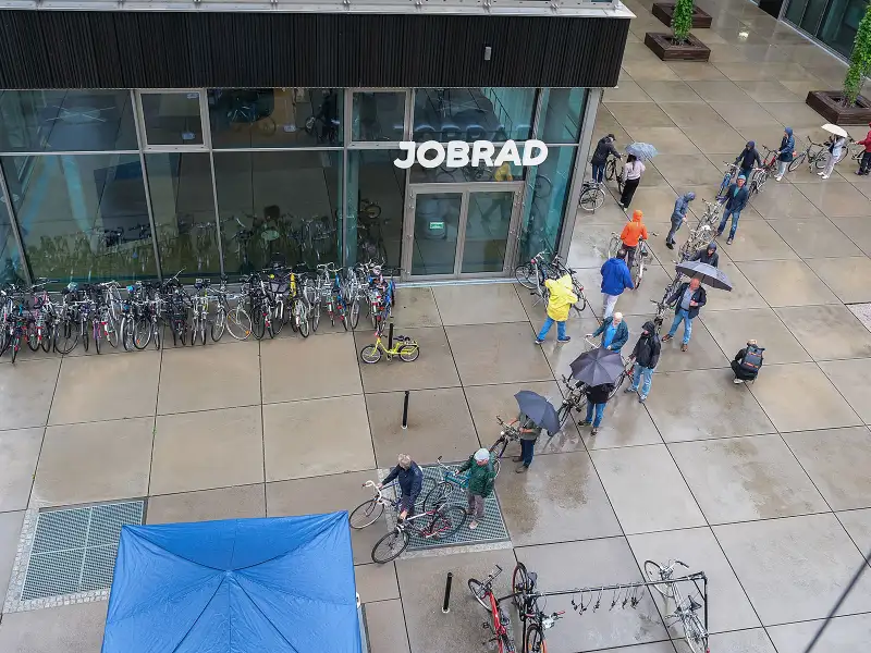 Eine lange Schlange von Menschen mit Fahrrädern und Regenschirmen auf dem JobRad Campus Eine lange Schlange von Menschen mit Fahrrädern und Regenschirmen auf dem JobRad Campus